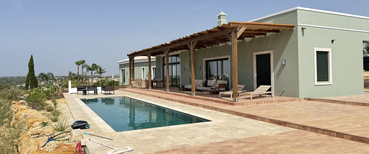Single-storey sage-green villa with a timber pergola and pool under a clear sky, in Quelfes