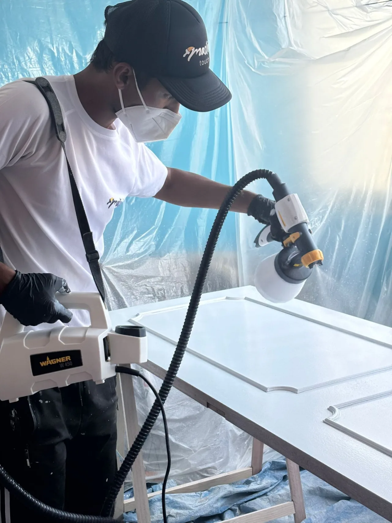 Painter in protective equipment spray-lacquering a door