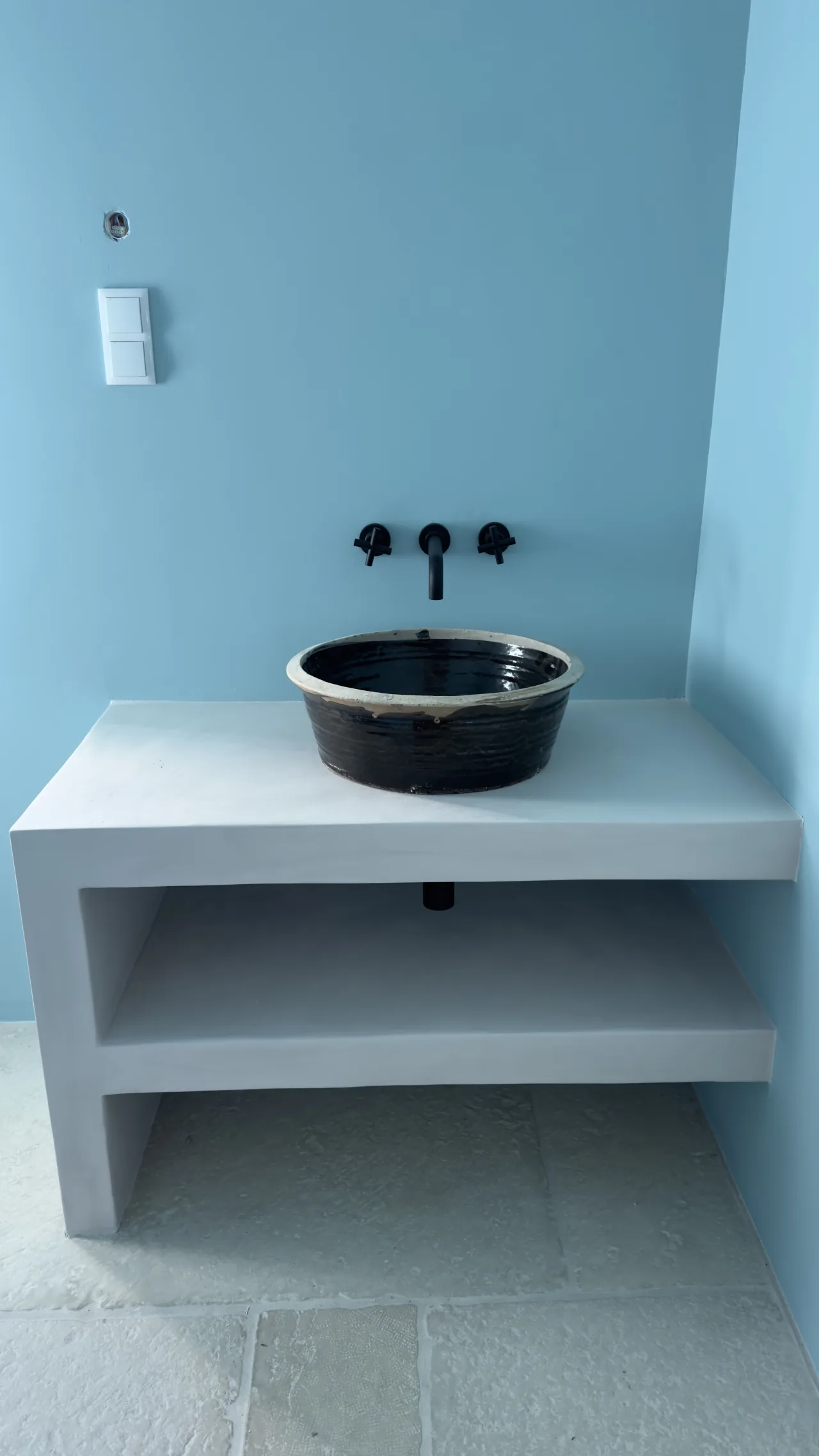 White microcement vanity with a dark ceramic basin, in a bathroom with blue walls