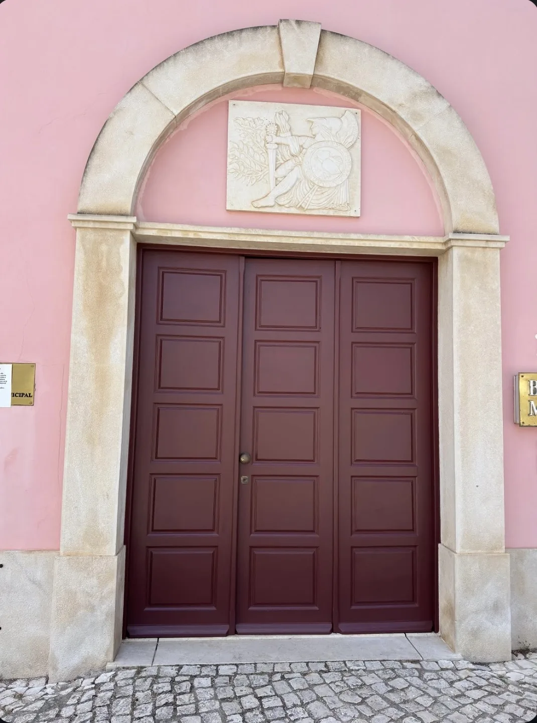 Burgundy main timber door beneath a stone arch, on a pink façade