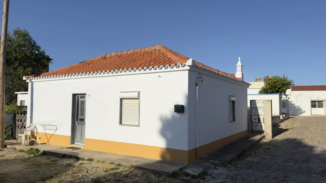 Hip-roofed house painted white, with an ochre band along the base and roller shutters