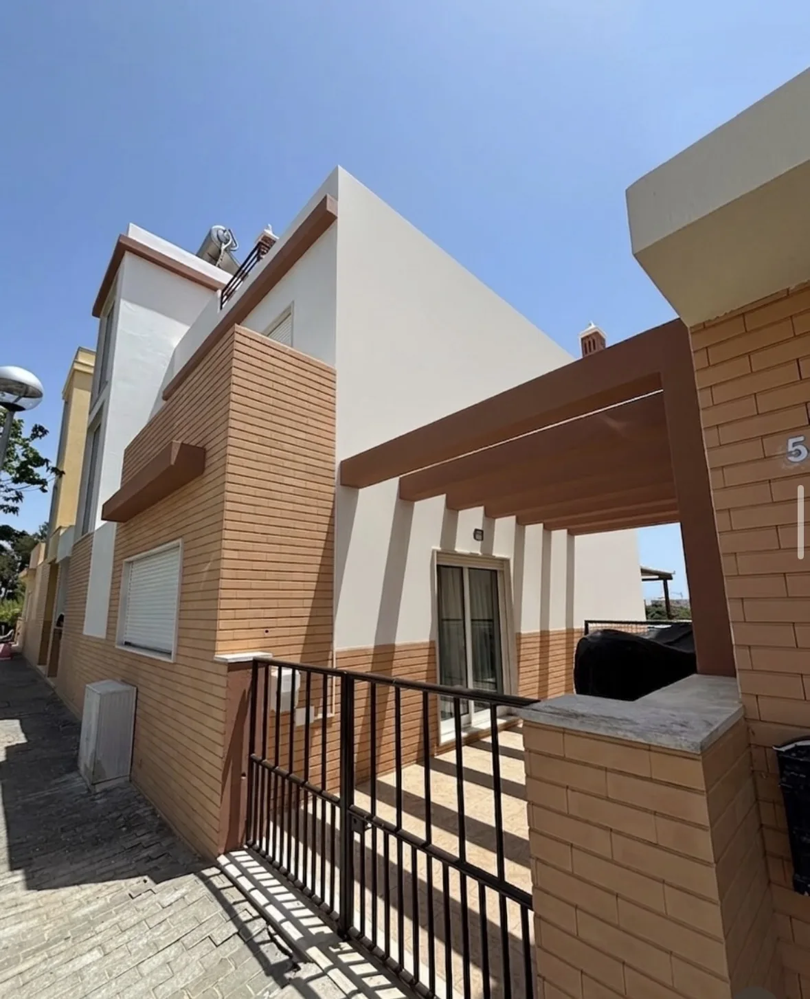 Entrada com pérgula castanha, fachadas brancas e revestimento cerâmico