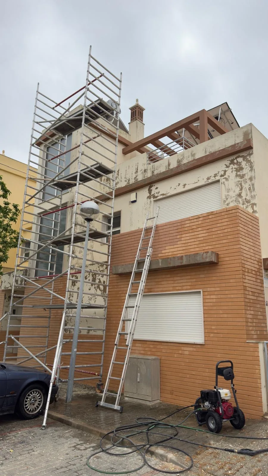 Fachada com o reboco a descascar, andaime montado e máquina de lavar a alta pressão