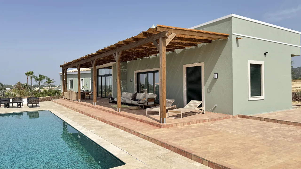 Single-storey sage-green villa with a timber pergola, sun loungers and a pool