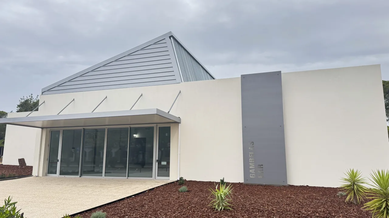 Gambelas Bar building with off-white façades, a metal canopy and a bark-mulch planting bed