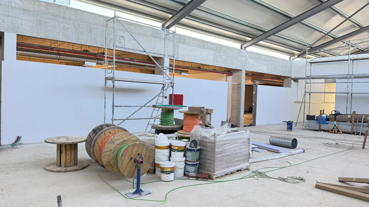 Interior em obra, com paredes pintadas de branco, andaime e latas de tinta